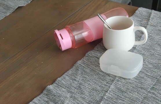 Items on a table including a container, a cup, and a bottle in a simple setting. dishes left behind after a meal