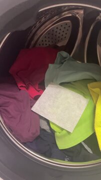 Vertical close up view of white color collector sheet lying on top of bright clothes inside modern washing machine drum before laundry cycle. High quality 4k footage