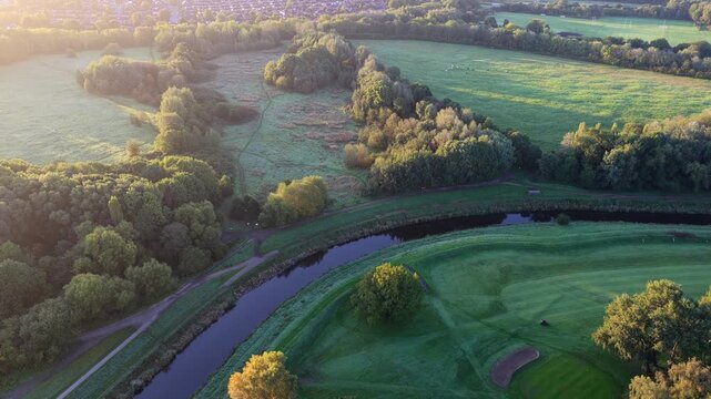 Aerial video capturing the blue River Mersey meandering past Didsbury Golf Course fairways, Stenner Woods, and dewy Millgate Fields at sunrise.