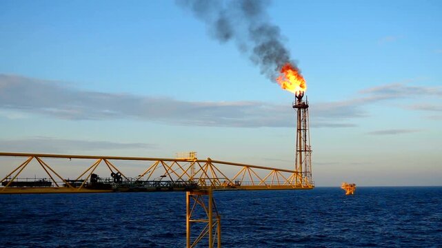 Offshore Oil and Gas Platform with Burning Flare Stack Over the Ocean at Dusk