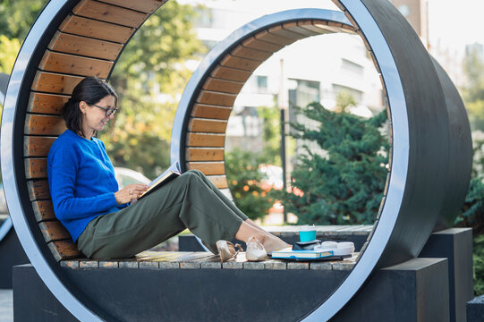 Businesswoman reads a book on a circular wooden bench outdoors