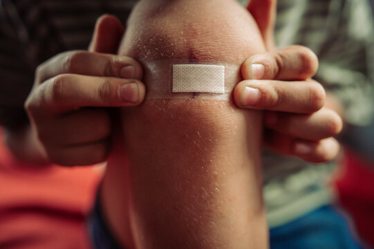 A boy applies an adhesive bandage to a wound on his knee