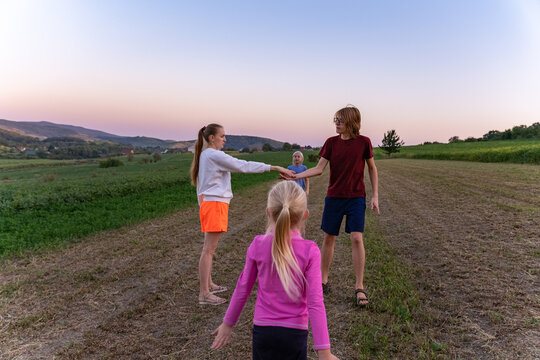 Mother and three children playing together in a rural field at dusk, bonding in warm sunset light, enjoying carefree childhood moments and quiet outdoor freedom