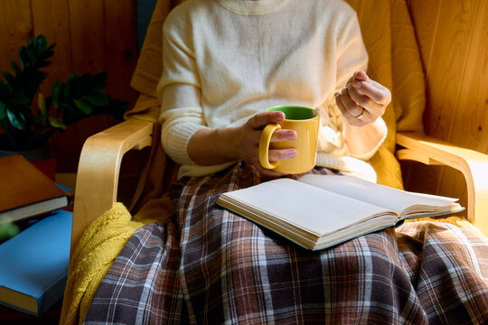 Woman sits in an armchair reading a book and holding a cup of tea