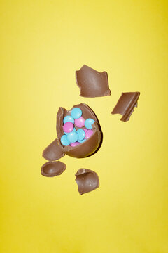 A broken chocolate easter egg contains colorful candy on yellow