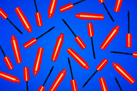 Red mascara tubes and wands are scattered on a blue background