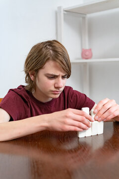 Young boy concentrating as he arranges white blocks on a wooden table, practicing fine motor skills, problem solving and creative construction during focused play indoors
