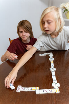 Children playing a game of dominoes at home, concentrating on placing the next tile on the table, enjoying family time and developing cognitive skills