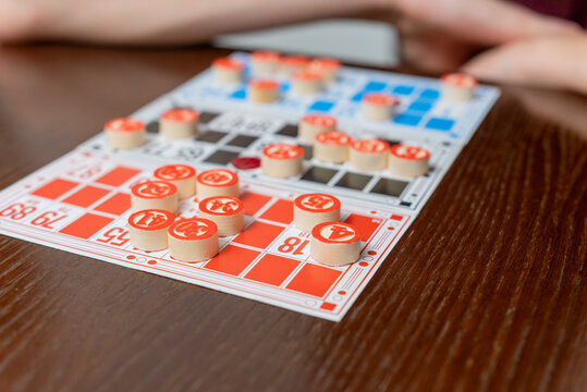 People gathered around a dark wooden table playing bingo, placing wooden number tokens on cards in a cozy social game night full of laughter, chance, and friendly competition