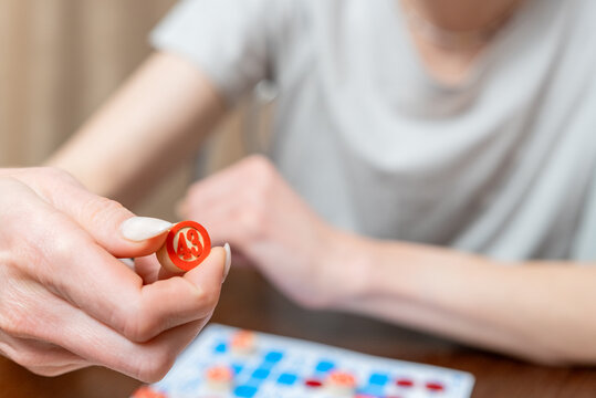 Woman's hand holding a red wooden number 43 marker during a bingo game, with a blurred game card visible on a wooden table, representing chance, luck, and entertainment