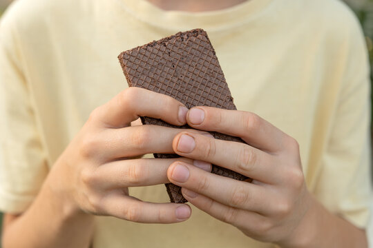 Young person's hands holding a rectangular chocolate wafer, showing the patterned surface and layering, creating a simple moment of enjoying a sweet snack