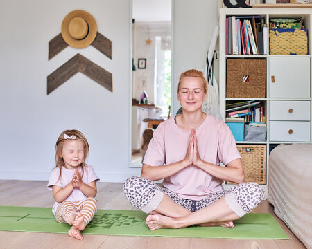 Mother and daughter meditating together on a yoga mat at home
