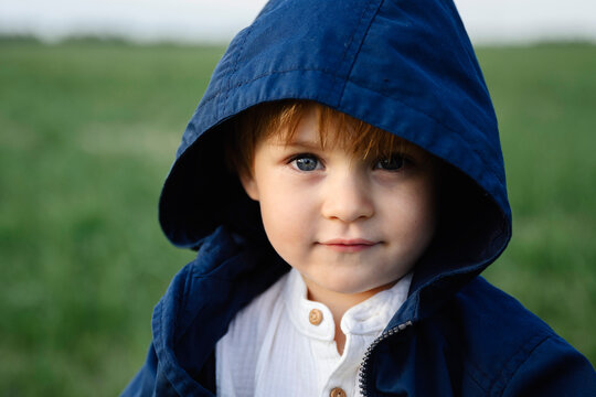 A boy wearing a blue coat looks at the camera in nature