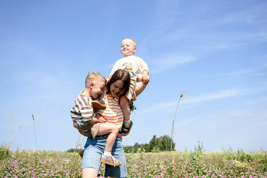 Smiling mother carries her sons in a summer flower field
