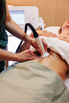 Cosmetologist performs radiofrequency body treatment on woman indoors