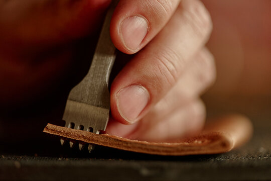 Male hand presses a metal tool into brown leather