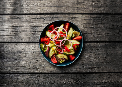 A fresh vegetable salad sits on a dark wooden table