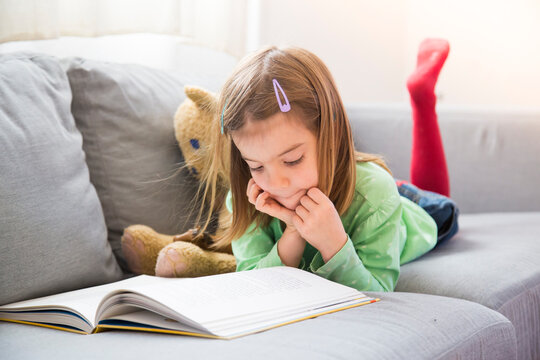 Little girl lying on couch watching book