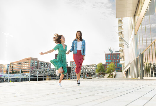 Carefree woman in dress runs with friend in Hamburg city during day