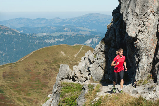 Austria, Kleinwalsertal, Young woman running on mountain trail near rocks