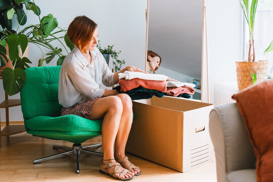 Thoughtful woman packing clothing into a cardboard box at home