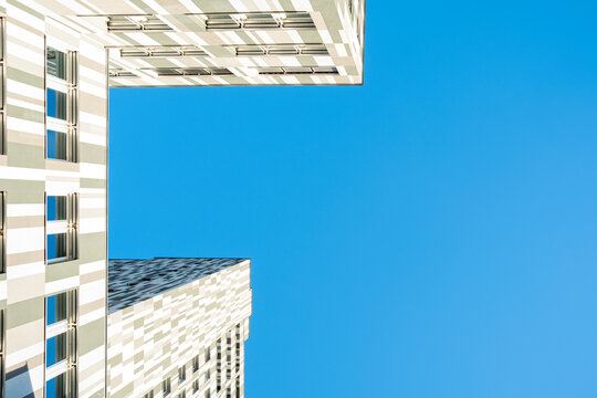 Upward view between modern skyscrapers and buildings against blue sky emphasizes facades geometry vertical scale and urban architecture