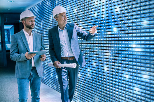 Two engineers analyze digital data on a large screen indoors