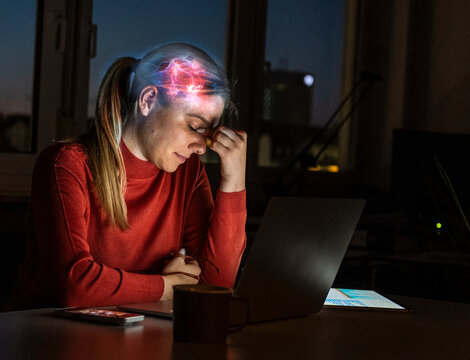 Tired woman with glowing brain hologram uses laptop