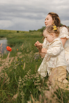 Mother and daughter look at a red poppy in a meadow