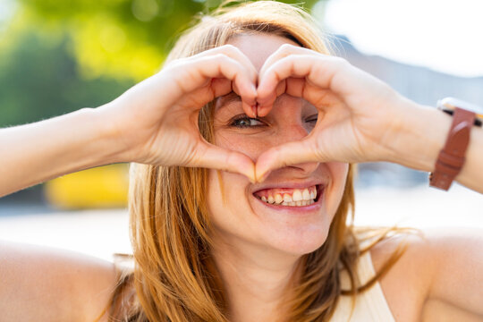 A smiling woman forms a heart shape with her hands outdoors in Berlin