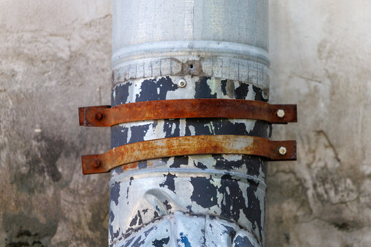 Rusted metal band secures weathered pipe to rough wall