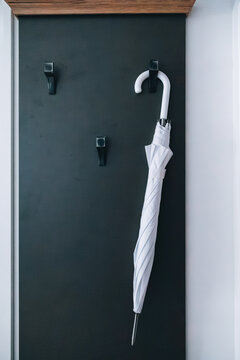 Home decor and lifestyle concept: white umbrella hung on a hook against a dark door in a minimalist entryway.