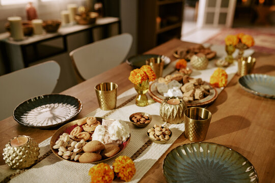 Festive table arrangement featuring traditional sweets, nuts, candles, and marigold flowers celebrating festival of lights. Useful for cultural holiday marketing campaigns