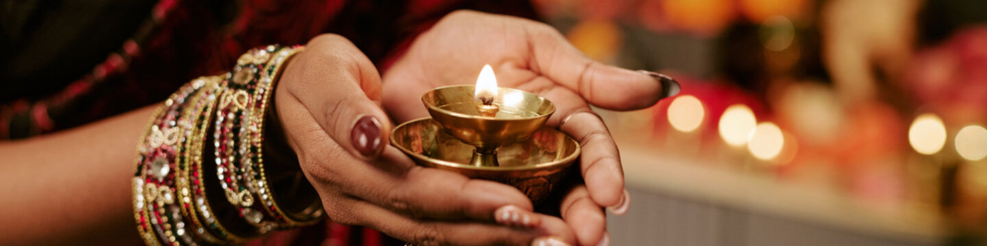 Header close up shot of Indian woman hands holding traditional burning oil lamp during festival celebration. Visual suitable for cultural holiday marketing campaigns