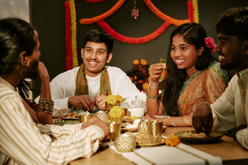 Obraz premium Asian Indian young adults and teenager smiling, celebrating traditional festive holiday together at dining table. Concept suitable for cultural marketing and holiday advertising campaigns