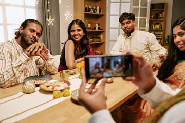 Obraz premium Young adult Indian friends posing for smartphone photo during cultural holiday dinner. Image suitable for mobile technology advertising, social media campaigns, lifestyle marketing