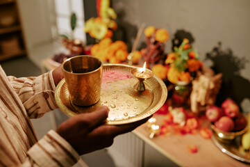 Obraz premium Cropped hands of Indian young adult man holding traditional brass pooja thali with burning oil lamp during Diwali celebration. Useful for festive religious marketing and cultural projects