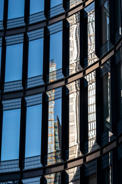 Reflection of a historic building appears across a modern glass facade where windows create contrast between urban architecture and the building