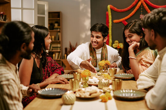 South Asian young adults sitting around table enjoying festive holiday meal together. Image portraying cultural lifestyle celebration suitable for holiday marketing campaigns
