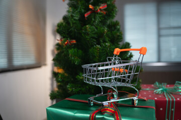 Small shopping cart on gift boxes in front of Christmas tree for holiday sale concept. © Oil And Den