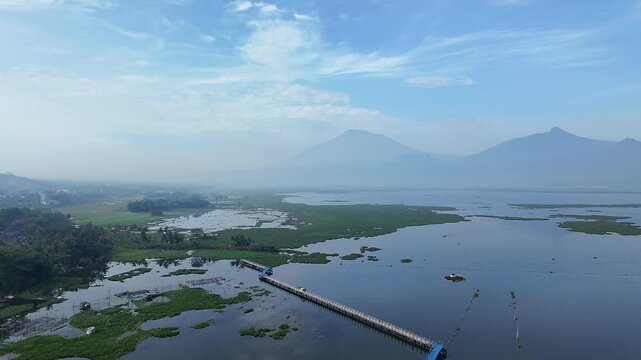 Beautiful aerial drone view of the Blue Bridge (Jembatan Biru Sumurup) at Rawa Pening lake with local village houses in Semarang, Central Java, Indonesia.
