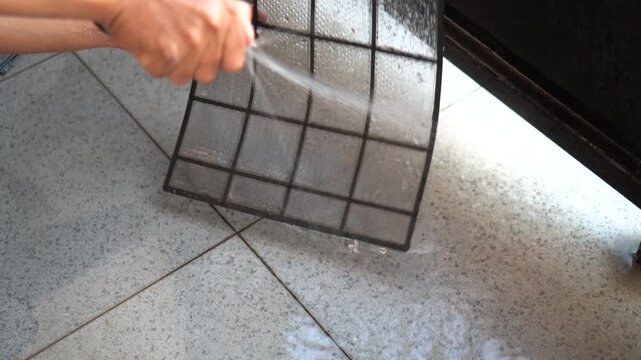 A man is manually cleaning his home air conditioner filter using a garden hose.