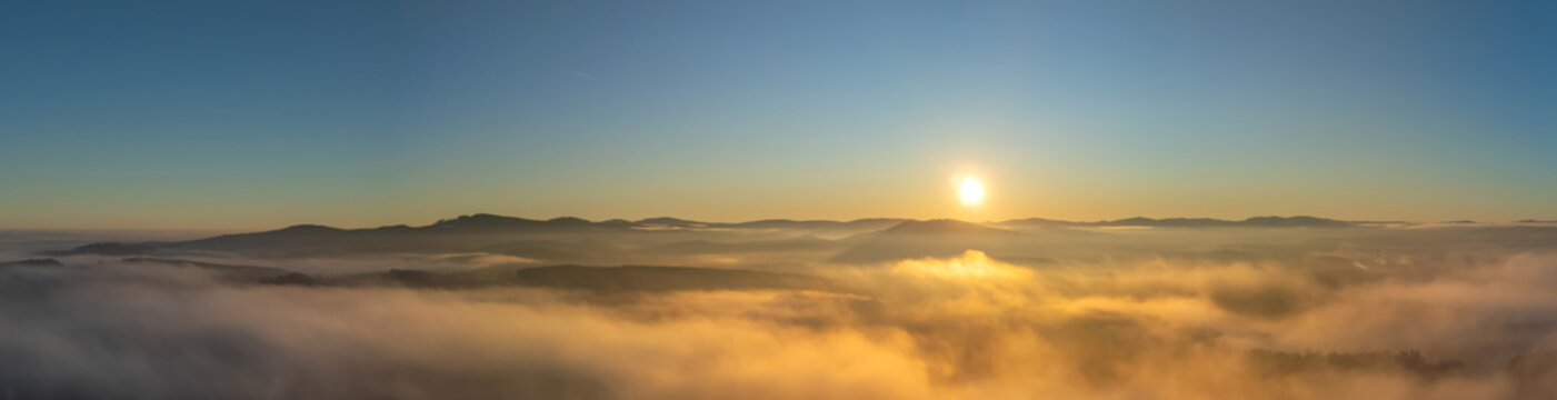 Panorama aerial view of a sea of fog over morning countryside under clear sky with sun