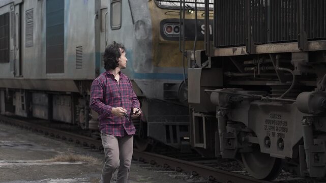 young Asian boy walking along the tracks next to an old passenger train at a rural railway station. Concept of travel, childhood journey, and transport.