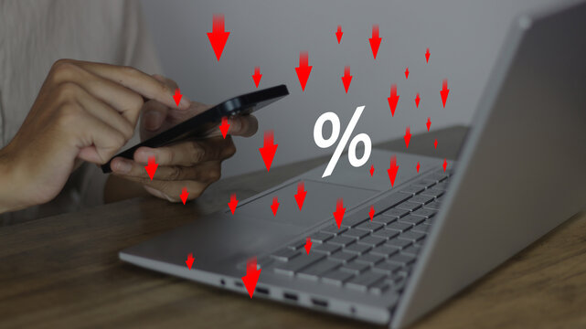 Show percentage icon with falling red arrows as a person uses a smartphone near a laptop, representing special offer of shopping department store discount, tax concept, lowering or adjusting interest 