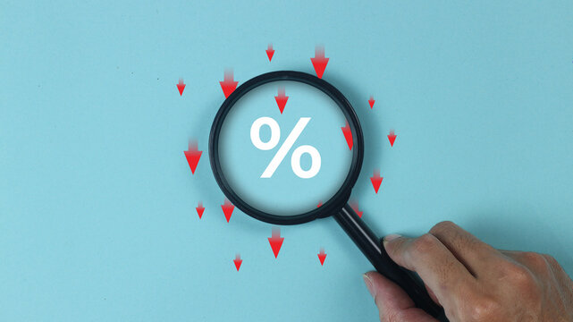 Showing percentage discount and interest rate reduction concept using a magnifying glass held by a hand, symbolizing price drop, tax cuts, shopping special offers, and financial market trends