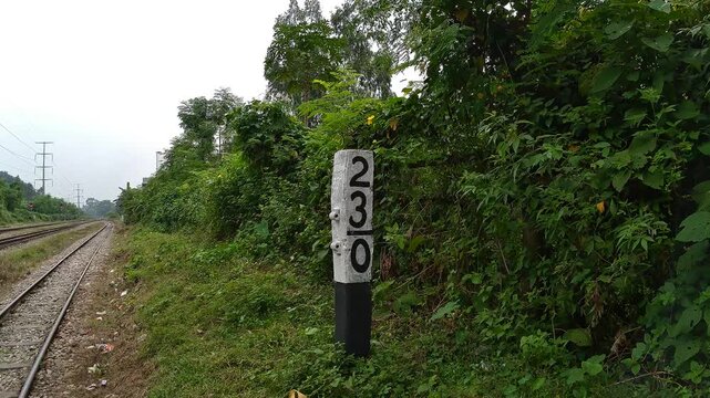 Railway kilometer marker post 230 beside tracks with green bushes