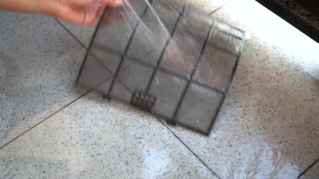 A man is manually cleaning his home air conditioner filter using a garden hose.