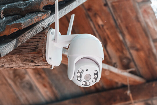 Mounted on a wooden beam exterior, a wireless security camera with IR LEDs and dual antennas watches over a rustic structure. Home security concept.