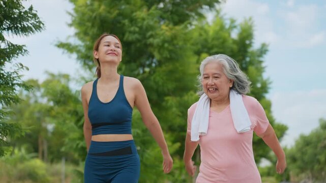 Two women walk side by side through a green park. Younger woman in blue athletic gear walks beside an older woman. The older woman wears pink